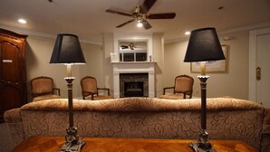 A room with a large bed, two standing lamps, a ceiling fan, a fireplace, and a wooden cabinet.