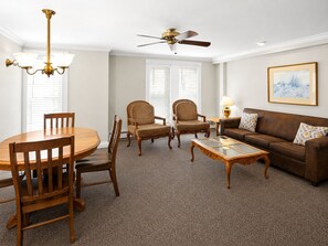 A living room with a round wooden table, two chairs, a sofa, and a ceiling fan.