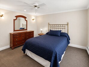 A bedroom with a bed, dresser, mirror, and ceiling fan.