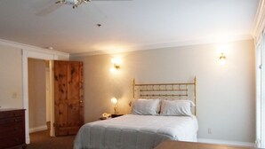 A bedroom with a bed, bedside lamps, a wooden door, and a ceiling fan.