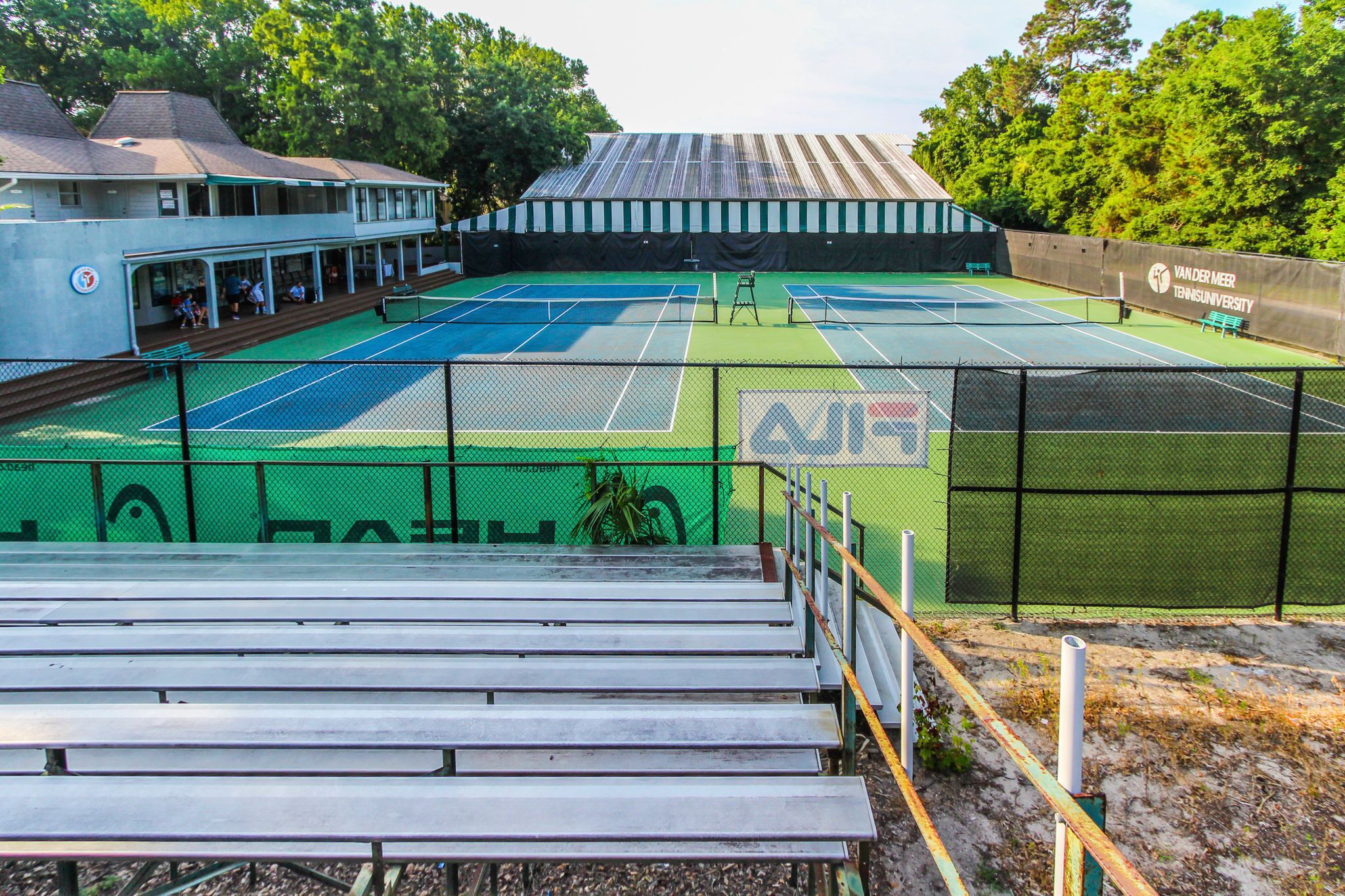 An outdoor tennis court with seating and a covered spectator area.