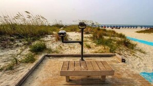 A wooden bench on a sandy path with binoculars on a stand, surrounded by beach grasses.
