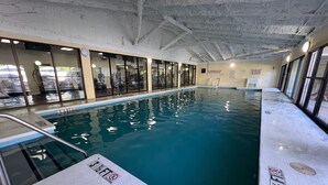 An indoor swimming pool with clear water, glass walls, and a ceiling with exposed beams.