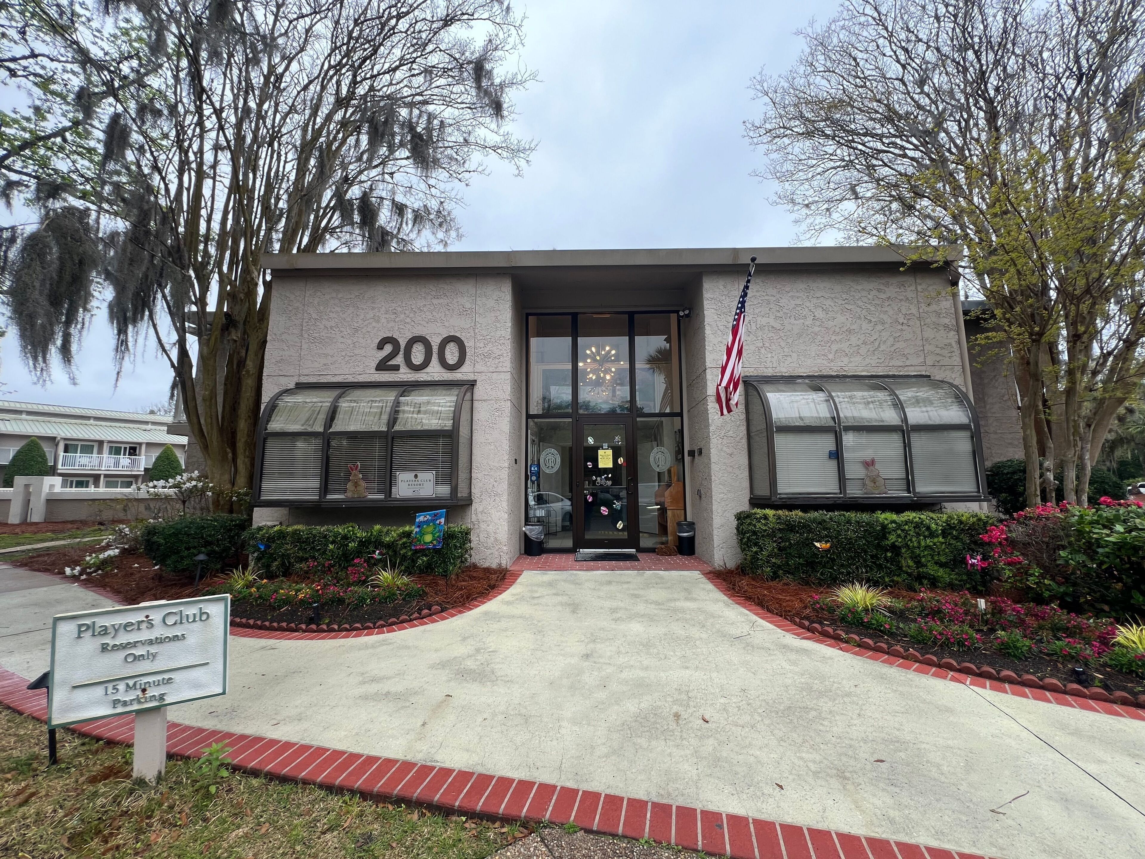 A building with the number 200 on its facade, a sign indicating it's a Player's Club with 15-minute parking, and an American flag.
