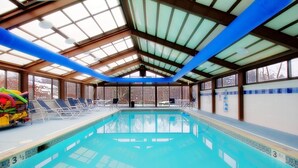 Una piscina interior con agua azul cristalina, rodeada de tumbonas y un techo de vidrio.