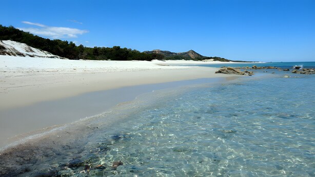 A beach with clear water, sandy shore, and rocky outcrops.