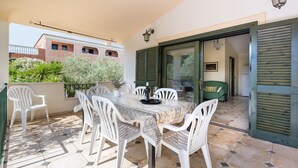 A balcony with a table and chairs, a view of a building, and a door with shutters.