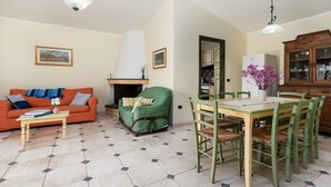 A living room with a sofa, a dining table with chairs, a fireplace, and a kitchen area.