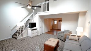 A spacious living room with a staircase, a flat-screen TV, and a comfortable seating area.