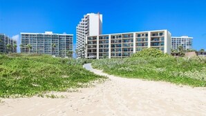 A beachfront hotel with multiple buildings, a sandy path leading to the beach, and lush greenery.