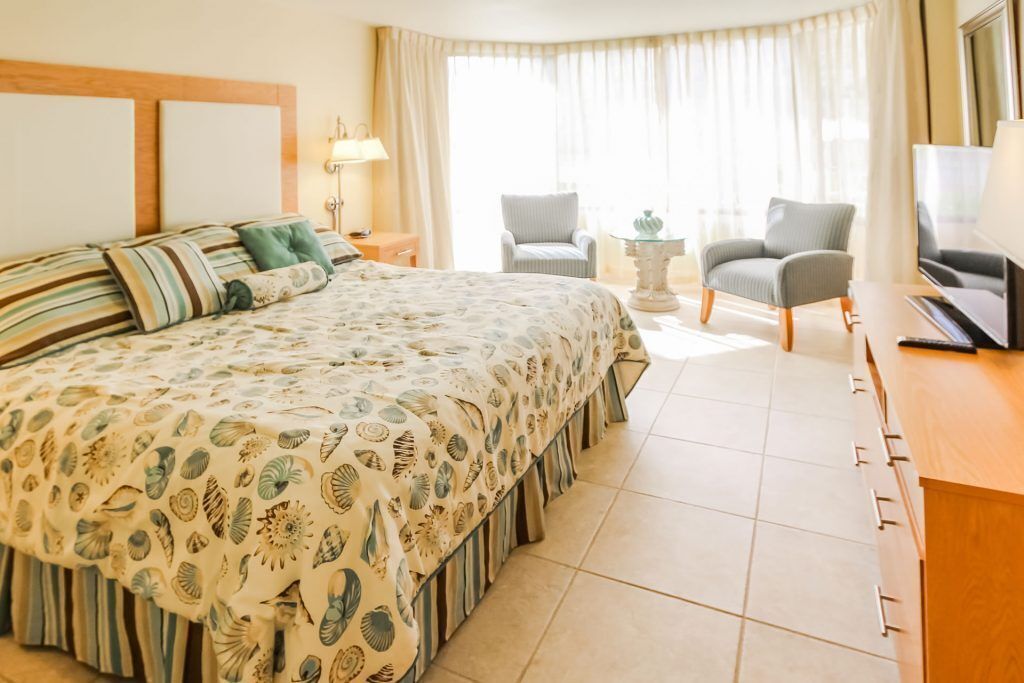 A hotel room with a large bed, two chairs, a small table, and a TV.
