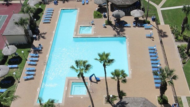 An aerial view of a resort with a large swimming pool surrounded by sun loungers and palm trees.