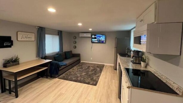 A modern living space with a sofa, a dining table, a kitchen area, and a flat-screen TV mounted on the wall.