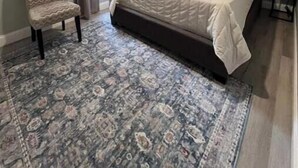 Un dormitorio con una cama grande, una silla, un tapete y un ventanal con cortinas.