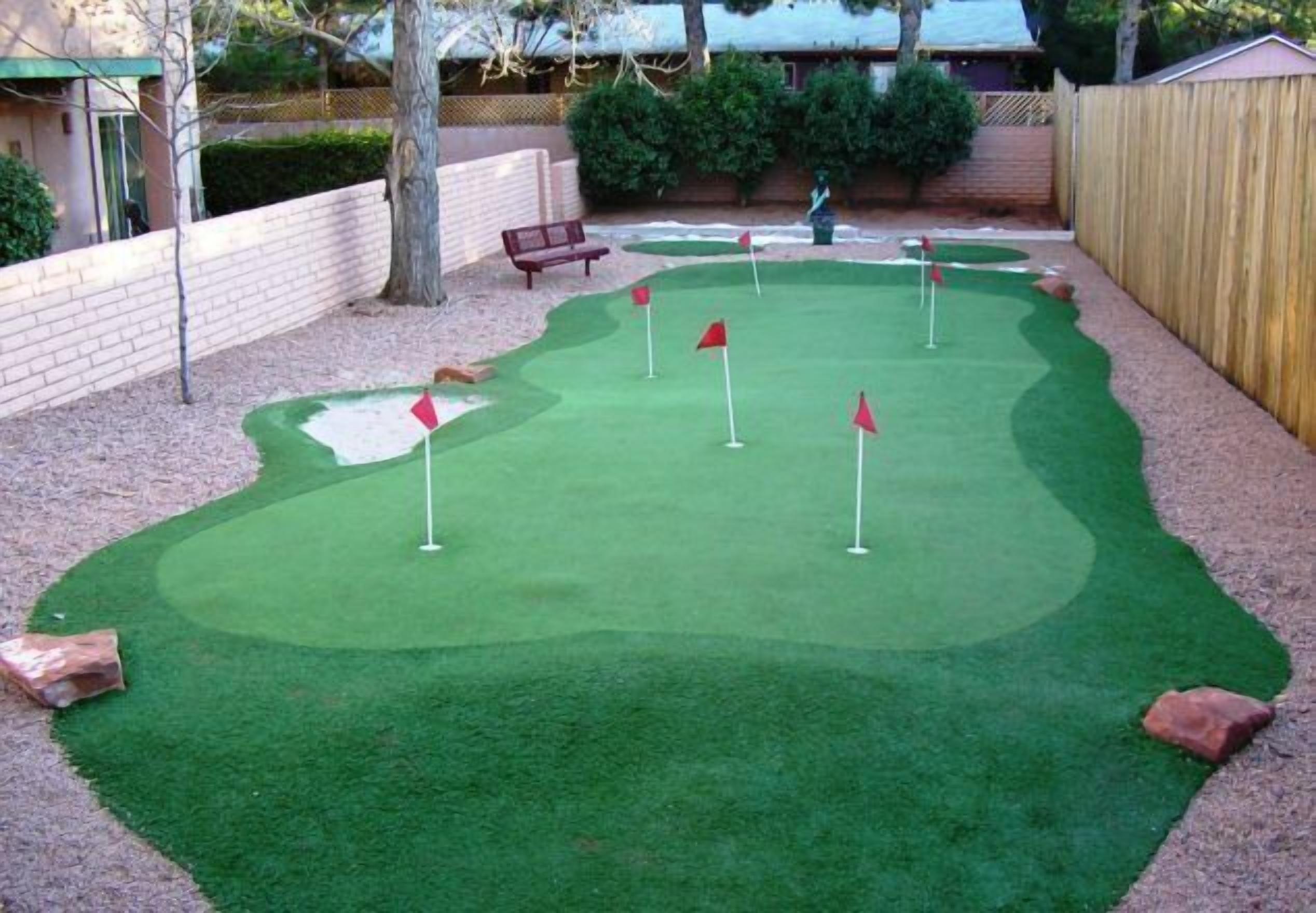 A miniature golf course with a green artificial turf, red flags marking the holes, and a wooden fence surrounding the area.