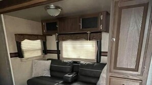 A compact RV interior with a sofa bed, a small cabinet, and a window with blinds. - RV camper in a peaceful place (Lake Panasoffkee)
