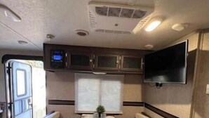 A compact RV interior with a dining table, two bench seats, a mounted TV, and a small cabinet. - RV camper in a peaceful place (Lake Panasoffkee)
