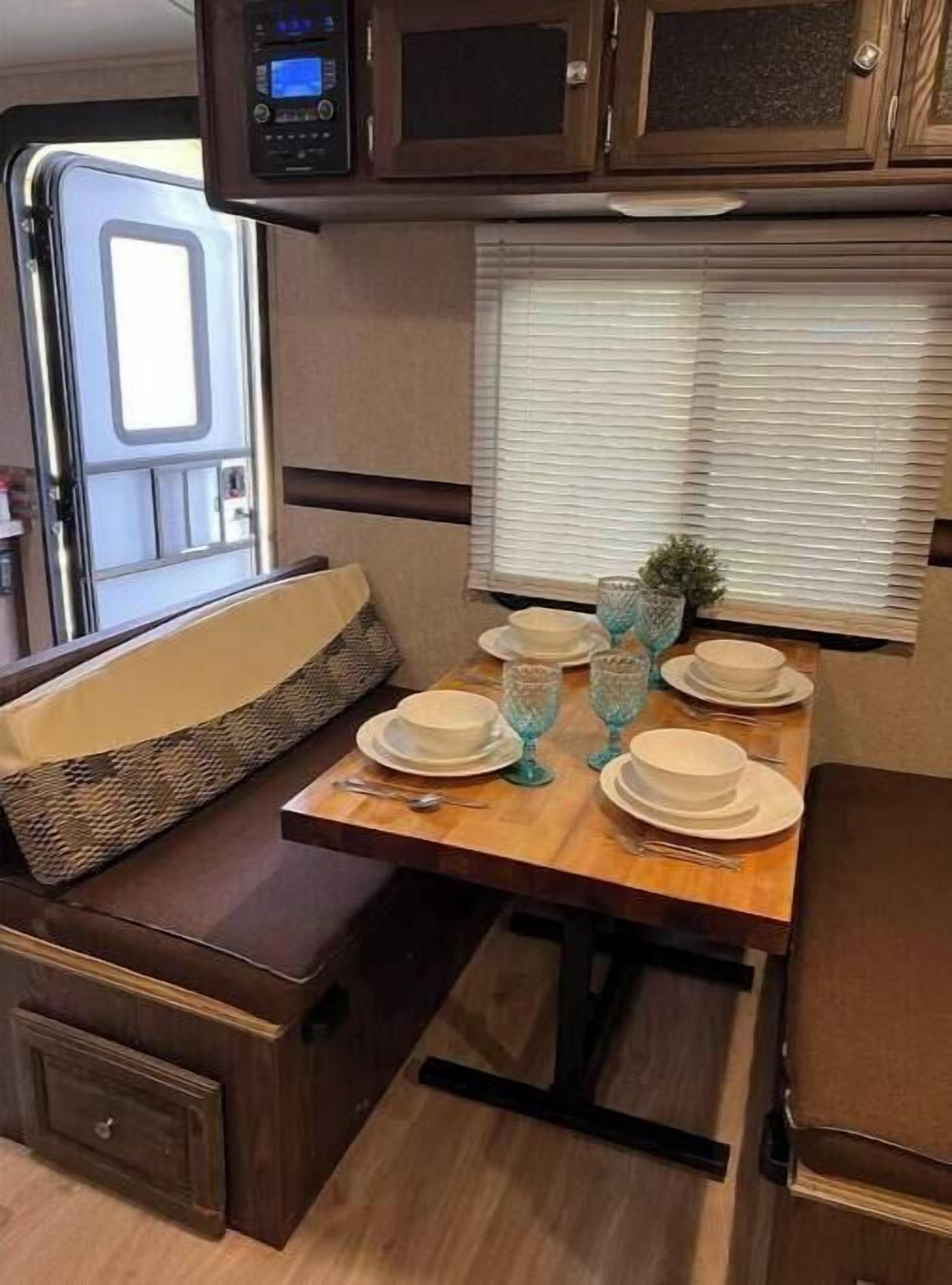 A compact RV kitchen with a dining table set for four, a microwave, and a window with blinds.