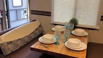 A compact RV kitchen with a dining table set for four, a microwave, and a window with blinds.