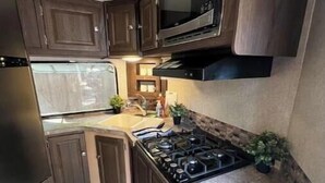 A compact RV kitchen with dark wood cabinets, a stainless steel refrigerator, a microwave, and a gas stove. - RV camper in a peaceful place (Lake Panasoffkee)