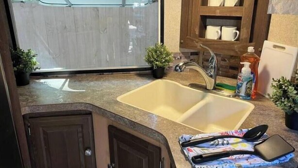 A compact RV kitchen with a double sink, wooden cabinets, a window, and a small countertop area. - RV camper in a peaceful place (Lake Panasoffkee)