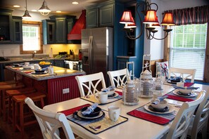 A kitchen with a central island, white chairs, and a dining table set for four. - 4-Bedroom Retreat near Silver Dollar City (Branson)