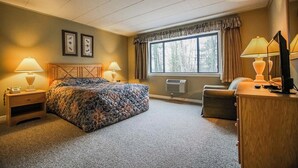 A bedroom with a bed, two bedside lamps, a nightstand, a dresser, a window with curtains, and a wall-mounted air conditioner. - 1-Bedroom Condo near Lake Wallenpaupack (Hawley)