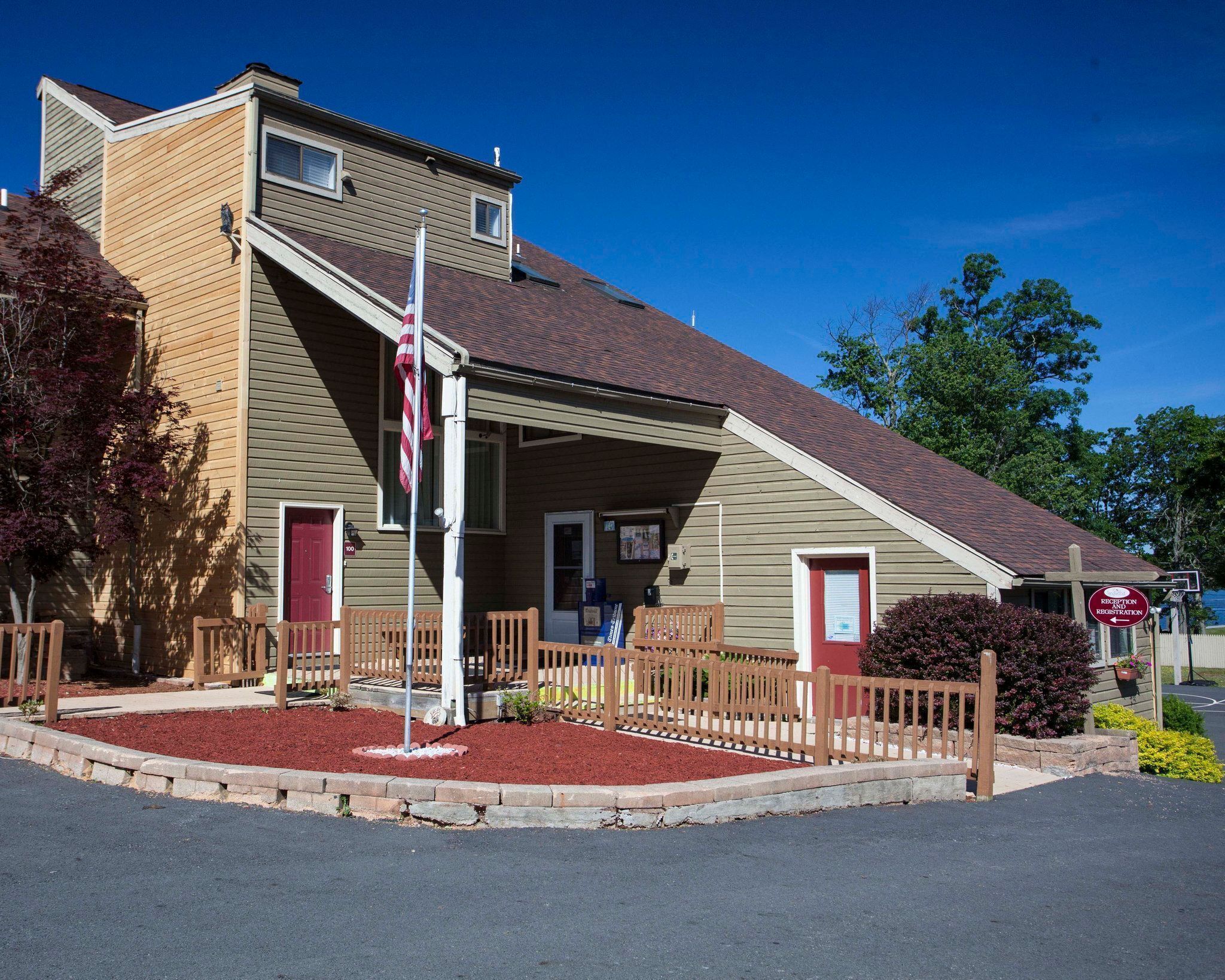 A two-story building with a sloped roof, a porch with a wooden railing, and a flagpole with an American flag.