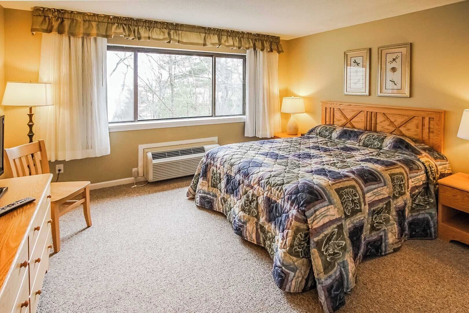 A bedroom with a large bed, two bedside lamps, a wooden headboard, a window with curtains, a desk with a chair, and a radiator.