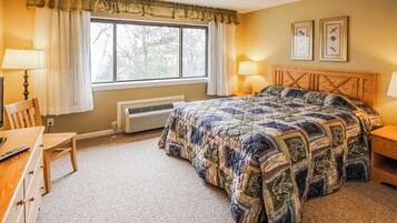 A bedroom with a large bed, two bedside lamps, a wooden headboard, a window with curtains, a desk with a chair, and a radiator.