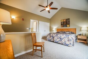 A bedroom with a bed, a chair, a desk, a ceiling fan, and a nightstand with a lamp.