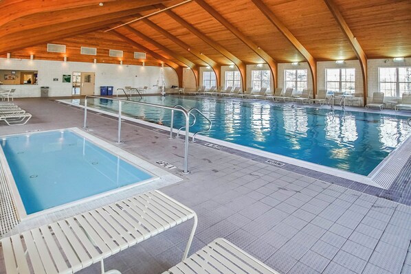 An indoor swimming pool with multiple lanes, lounge chairs, and a wooden ceiling.