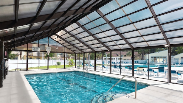 An indoor swimming pool with a glass ceiling, clear poolside chairs, and a lifeguard station.