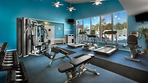 A gym with various exercise equipment, large windows, and ceiling fans.