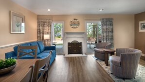 A living room with a blue sofa, a wooden dining table with chairs, a fireplace, and a large clock on the wall.