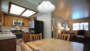 Una cocina con armarios de madera, microondas, estufa, refrigerador y un comedor con mesa y sillas de madera.