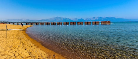 Una playa con agua cristalina, muelles de madera y montañas al fondo.