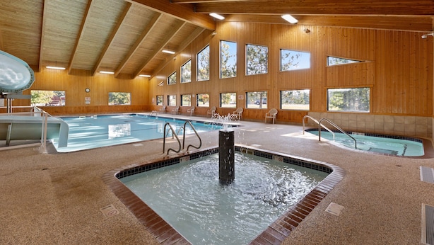 An indoor swimming pool with multiple lanes, a hot tub, and wooden walls with large windows.