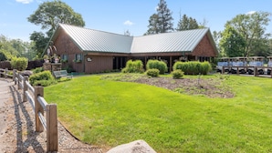 A rustic building with a metal roof, surrounded by a well-maintained lawn and a wooden fence.
