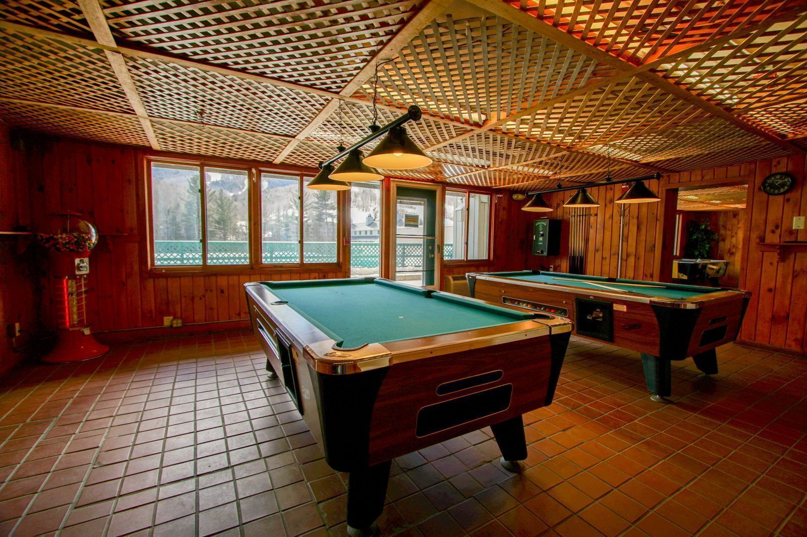 A pool room with two pool tables, wooden walls, and a ceiling with a lattice pattern.
