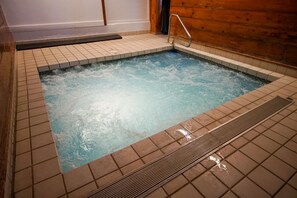 A hot tub with a tiled floor and a wooden wall.