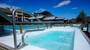 A hot tub with a metal ladder, surrounded by buildings with a mountainous backdrop. - Spacious 2BR Loft near Loon Mountain (Lincoln)
