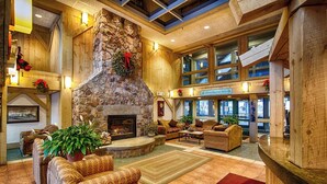 A spacious lobby with a stone fireplace, wooden walls, and a large window overlooking the interior. - Spacious 2BR Loft near Loon Mountain (Lincoln)