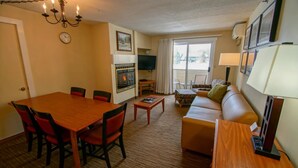 A cozy living room with a wooden dining table, red chairs, a sofa, and a TV. - Condo Nr Loon Mountain | King Bed + Balcony Views (Lincoln)