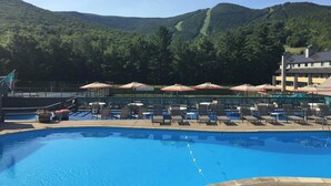 A swimming pool with lounge chairs and umbrellas, surrounded by a fence, with a mountainous backdrop. - Condo Nr Loon Mountain | King Bed + Balcony Views (Lincoln)