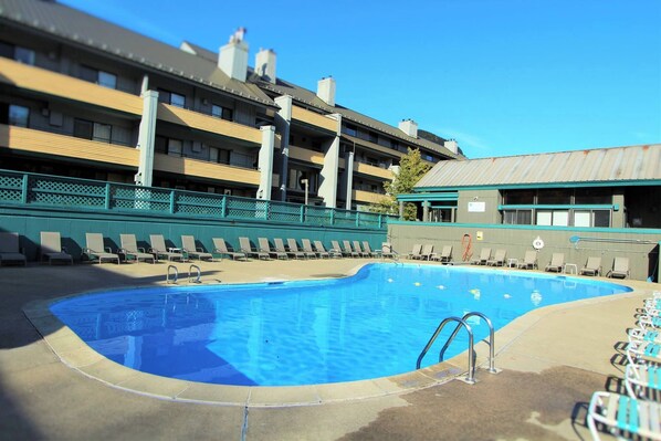 Une piscine avec des chaises longues et, au fond, un bâtiment doté de nombreux balcons.