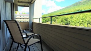 A balcony with two chairs and a table, overlooking a green landscape with hills. - Spacious Loft Condo Near Loon Mountain (Lincoln)