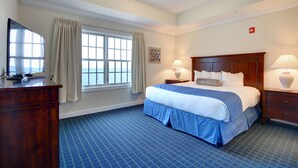 A hotel room with a large bed, a desk with a flat-screen TV, a window with curtains, and a lamp on the nightstand. - Waterfront 2BR Condo with Stunning Sound Views (Roper)
