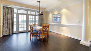 A dining area with a table and chairs, a large window with curtains, and a view of the outdoors. - Waterfront 2BR Condo with Stunning Sound Views (Roper)