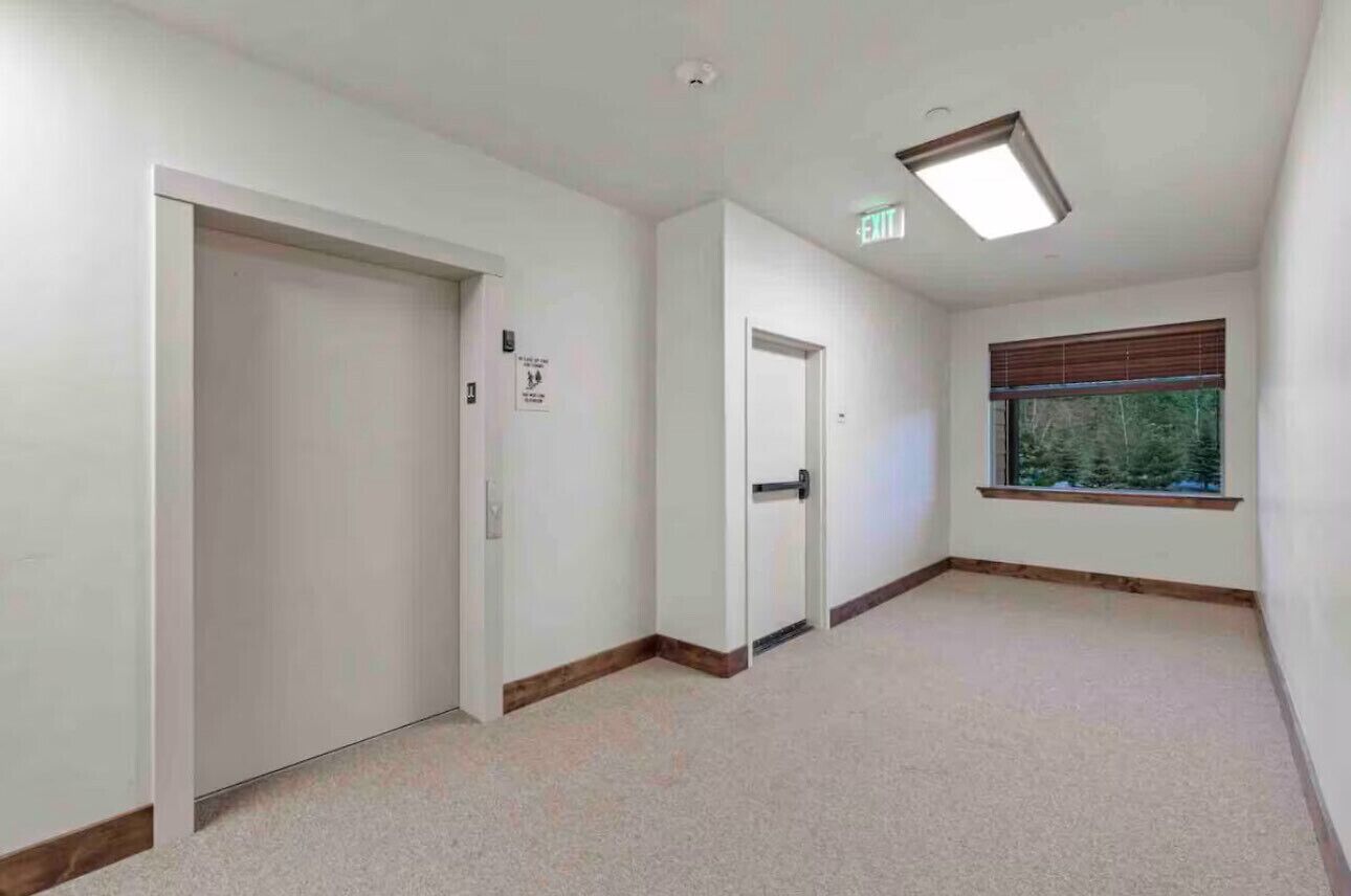 A hallway with two doors, one of which is a sliding door, and a window with a view of trees.